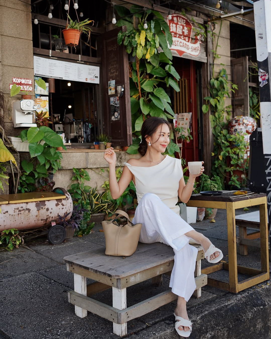 Woman sitting on a wooden bench in front of a cafe, holding a cup.